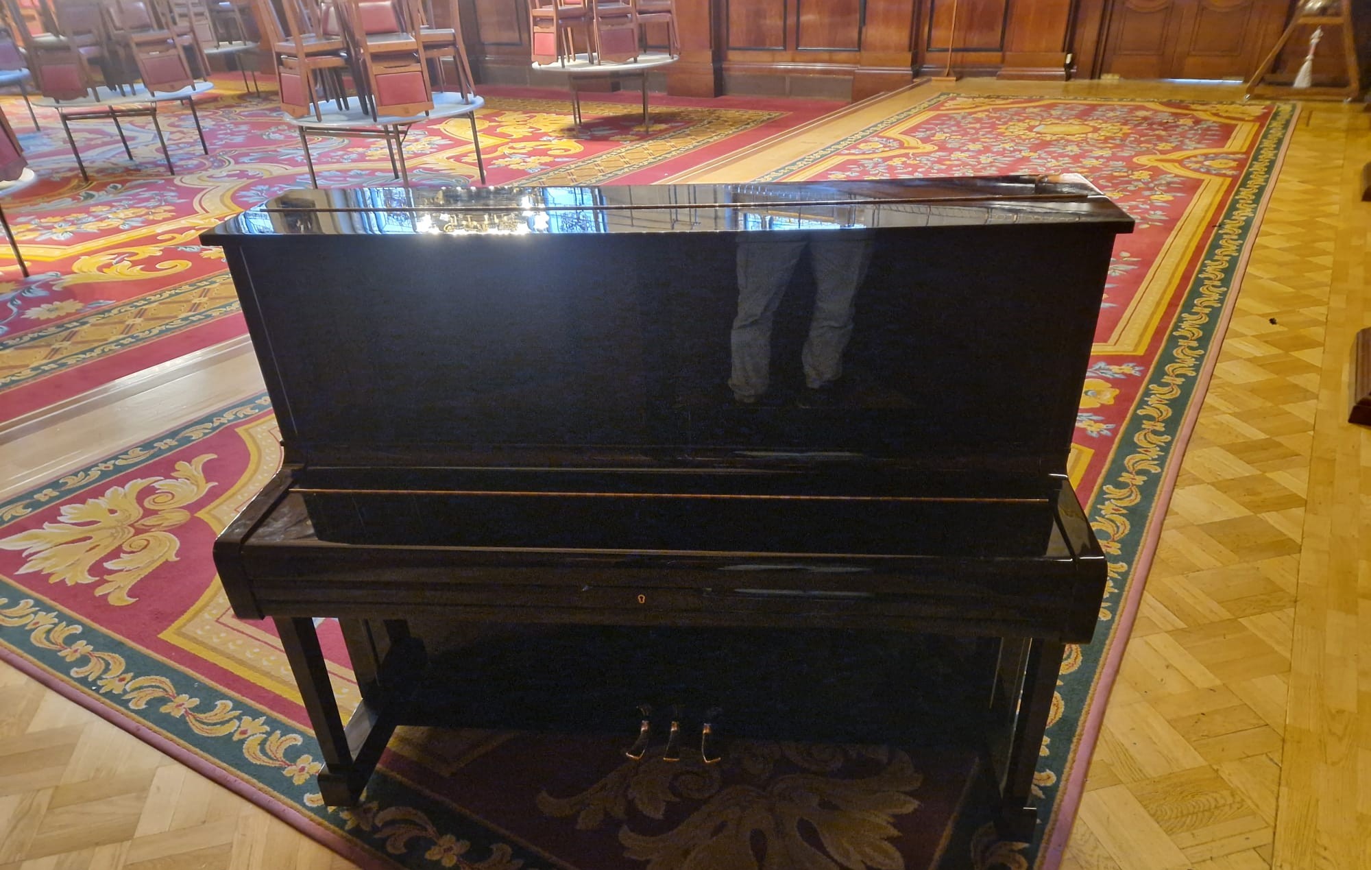 Glossy black upright piano in a home setting with patterned carpet.